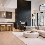Bright modern Austin luxury home interior featuring an open concept kitchen and living room with a black marble fireplace wall, large floor to ceiling windows, light wood floors, and contemporary minimalist design.
