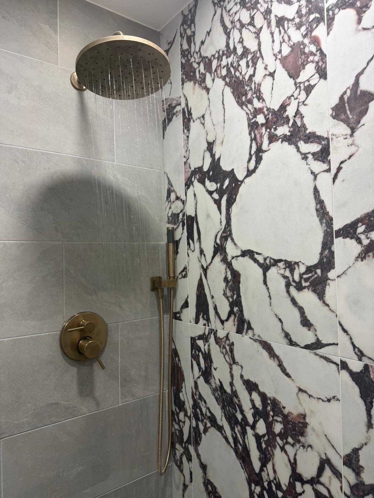 Completed bathroom remodel in Hutto TX with marble look tile shower and gold rain shower fixtures by B&H Remodeling