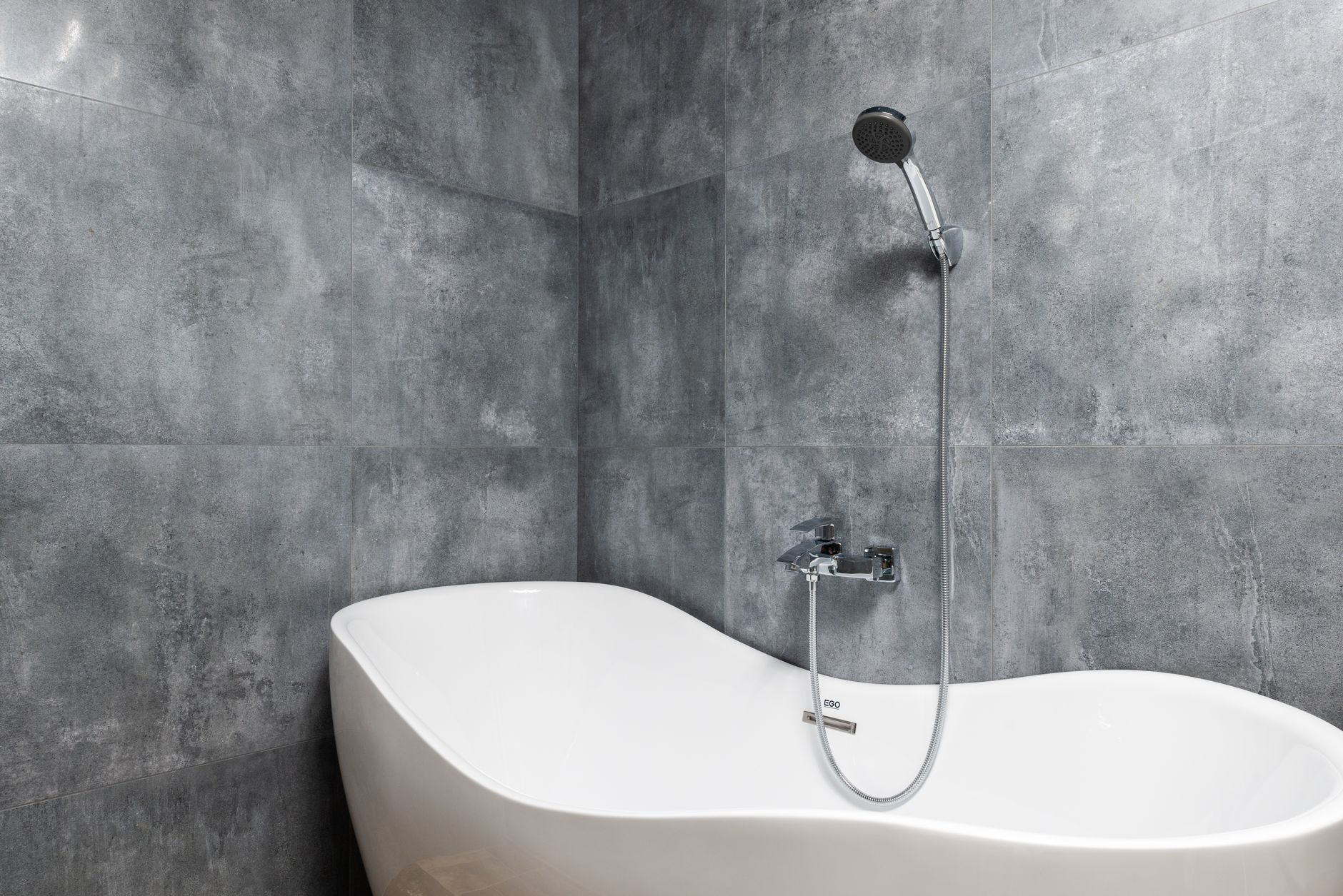 Modern white bathtub replacement with gray tile walls in a bright Austin bathroom remodel by BH Remodeling